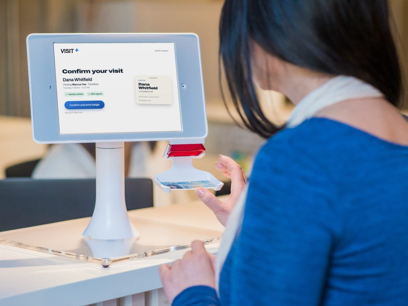 A visitor confirming her visit on a Visit+ check-in kiosk, with her badge shown ready to print